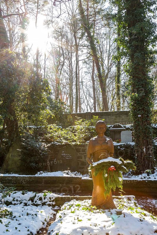 Female figure on a grave in the snow, sun from behind, Dresden Forest Cemetery, Saxony, Germany, Europe