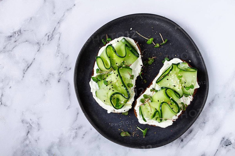 Breakfast, grain bread sandwiches, cream cheese, sliced cucumber, with microgreens, and sesame seeds, on a light table, close-up, top view, selective focus, no people