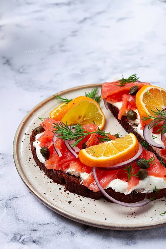 Sandwich with freshly smoked salmon, on black bread, with cottage cheese, with herbs and red onions, capers and pieces of citrus fruits, on a marble countertop, breakfast, no people