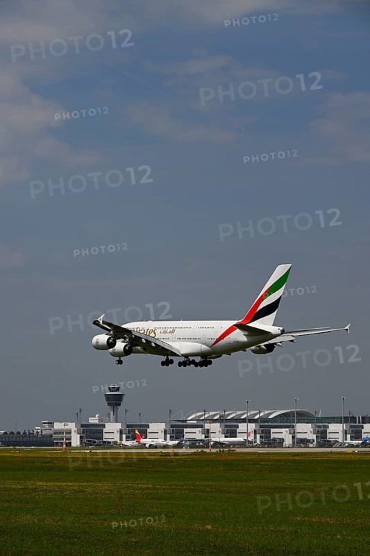 Emirates Airbus A380-800 approaching under blue sky, with control tower and Terminal 2 landing on southern runway, Munich Airport, Upper Bavaria, Bavaria, Germany, Europe