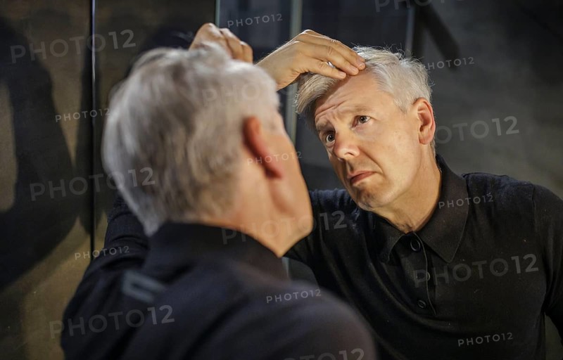 Symbolic photo on the subject of a high hairline and receding hairline. A man looks at his hairline in the mirror. Berlin, 13.08.2024
