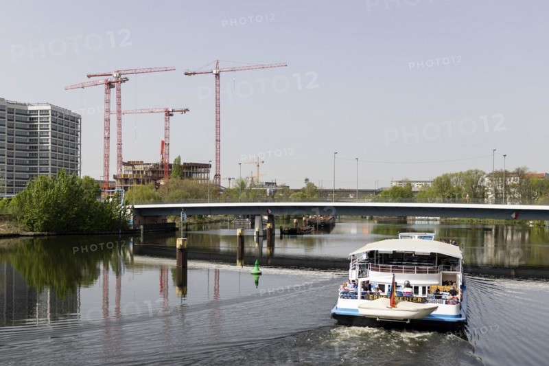 Four red construction cranes stand on a building site in Berlin's Heidestraße while a tourist boat sails across the Berlin-Spandau shipping canal, 08/04/2024