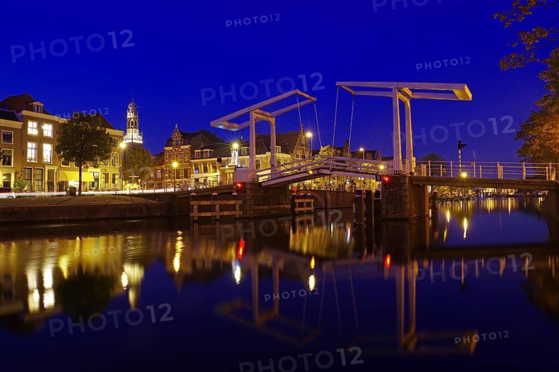 An illuminated canal with bridge and historic buildings in the background at night, evening mood, Haarlem, Netherlands