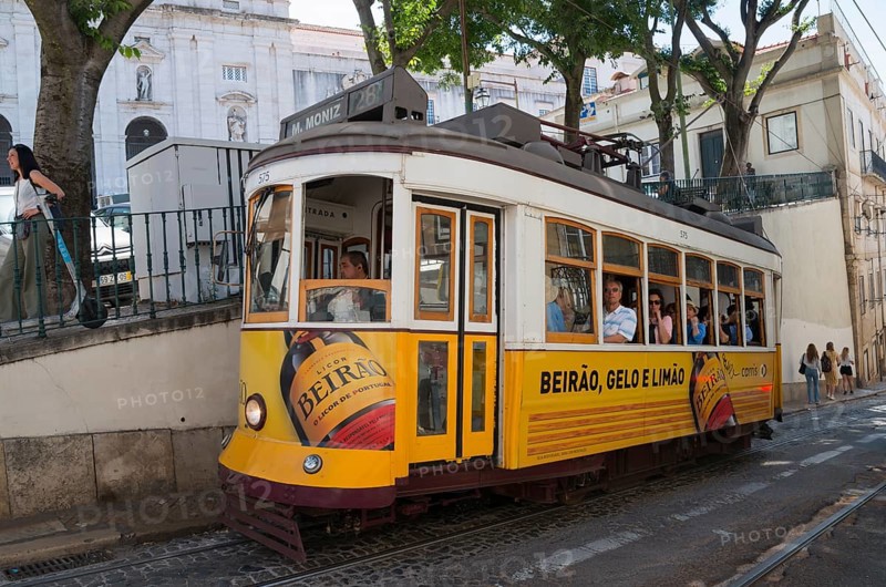A yellow tram with Beirão advertising runs through a narrow city street, people on board, tram, line 28, Carros eléctricos de Lisboa, Eléctricos de Lisboa, Old Town, Lisbon, Portugal, Europe