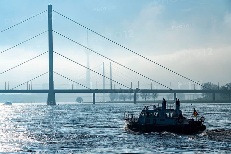 Dense fog slowly lifting, patrol boat of the water police on the Rhine near Düsseldorf, in front the Oberkassler Bridge, behind it the Rheinknie Bridge, Rhine Tower, North Rhine-Westphalia, Germany, Europe