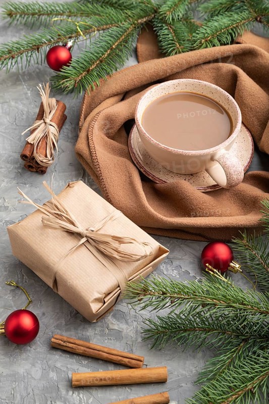 Christmas or New Year composition. Decorations, box, cinnamon, fir and spruce branches, cup of coffee, wool scarf on a gray concrete background. Side view, close up