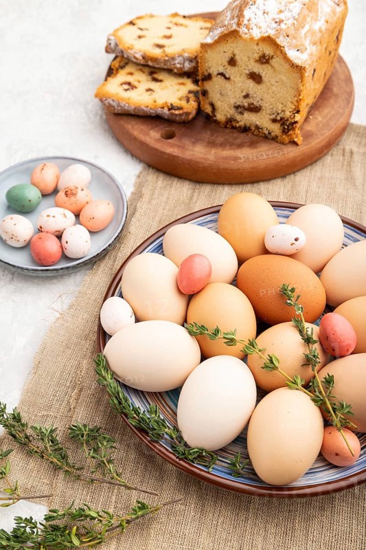 Homemade easter colored eggs on plate and raisins cake on a gray concrete background and linen textile. side view, close up