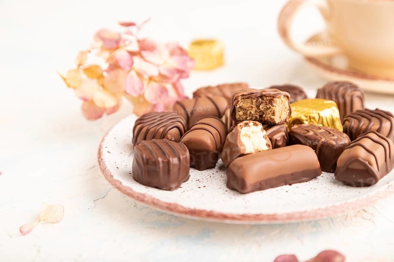 Chocolate candies with cup of coffee and hydrangea flowers on a white concrete background. side view, close up, selective focus