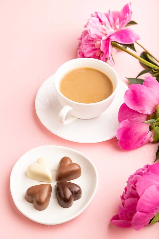 Cup of cioffee with chocolate candies, pink peony flowers on pink pastel background. side view, close up, still life. Breakfast, morning, spring concept