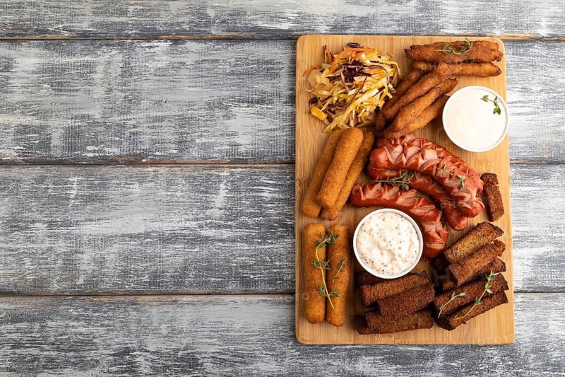 Set of snacks: sausages, nuggets, cheese sticks, toast, cabbage salad on a cutting board on a gray wooden background. Top view, flat lay, copy space