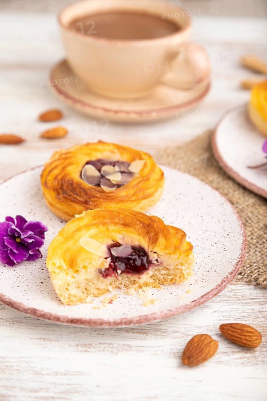 Small cheesecakes with jam and almonds with cup of coffee on a white wooden background and linen textile. Side view, close up, selective focus