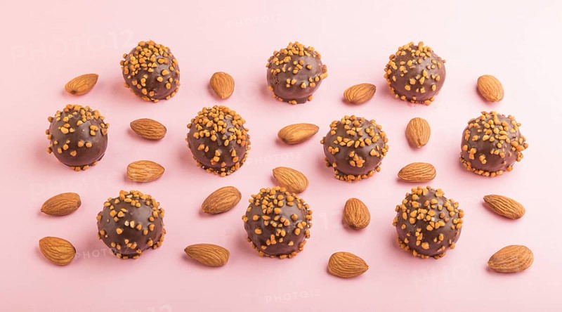 Chocolate caramel ball candies with almonds in a row on a pastel pink background. side view, close up