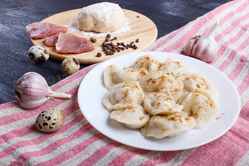 Dumplings on a plate with ingredients (meat, dough, spices) on a linen tablecloth on a black wooden background. close up