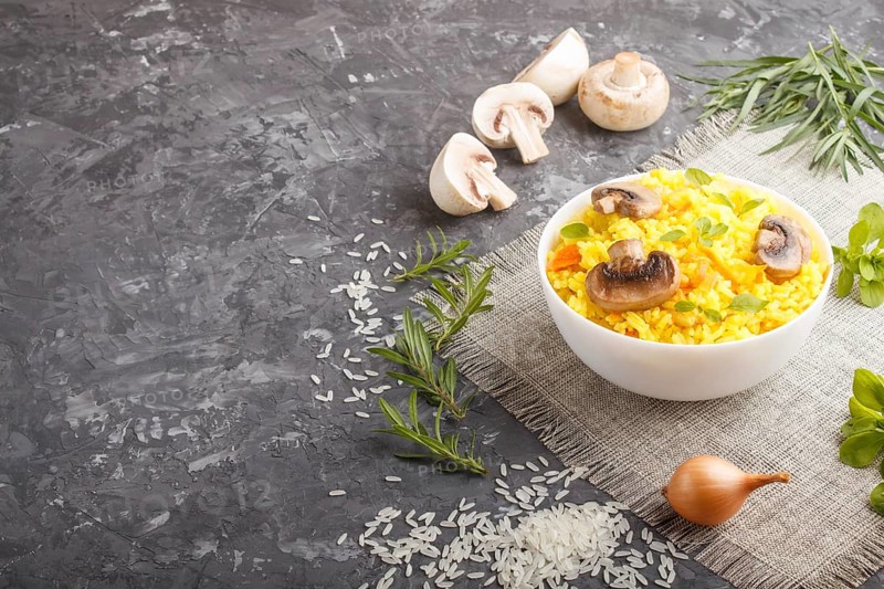Yellow fried rice with champignons mushrooms, turmeric and oregano in white ceramic bowl on a black concrete background. side view, copy space
