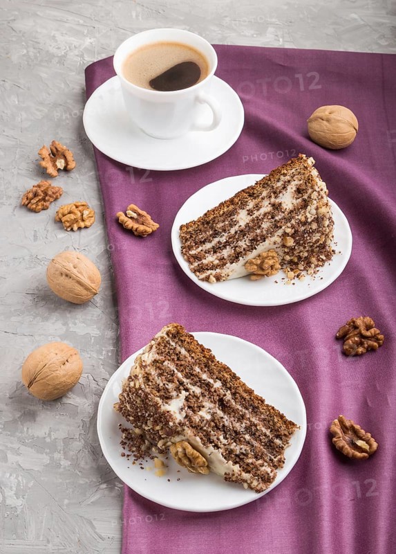 Homemade cake with milk cream and walnuts with cup of coffee on a gray concrete background and purple textile. side view, close up