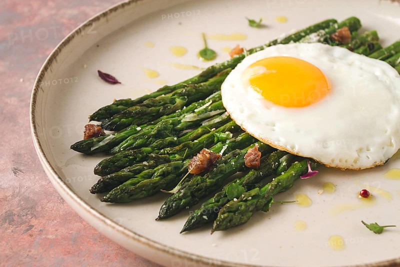Grilled asparagus, with fried egg, spices and herbs, parmesan cheese, on a beige plate, top view, rustic, no people