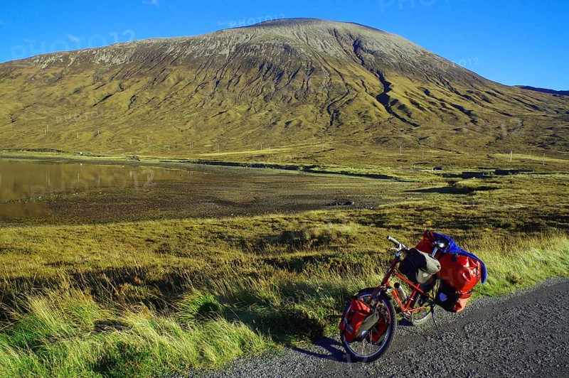 A loaded bicycle stands at the roadside in front of an impressive mountain landscape under a clear blue sky, Cycling tour, October, Hebrides, Isle of Skye, Hebrides, Scotland, Great Britain