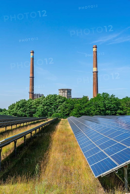 Solar modules of a solar park in front of the decommissioned Plessa lignite-fired power plant with two chimneys and cooling towers, Plessa, Lusatia, Brandenburg, Germany, Europe