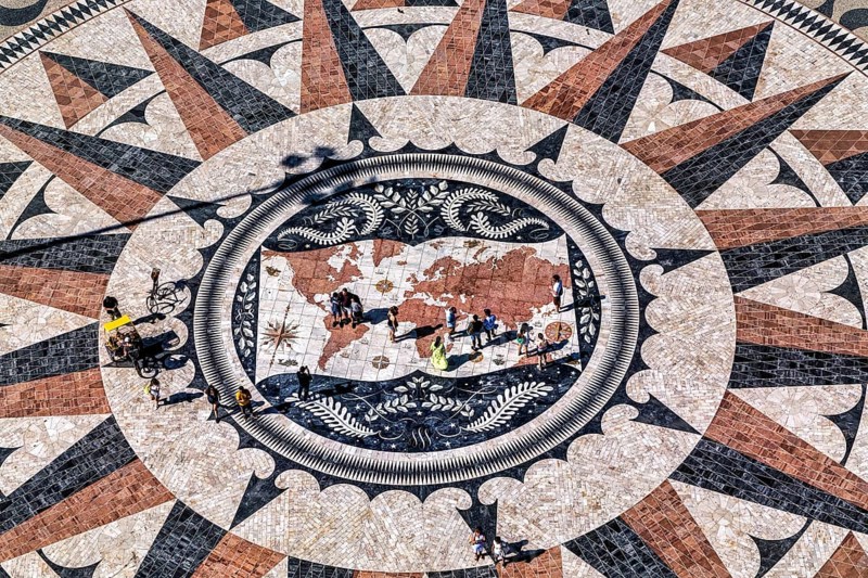 Ein Bodenmosaik mit einer Kompassrose und einer Weltkarte, umgeben von Menschenfiguren, die Entdeckungen symbolisieren, Lissabon
