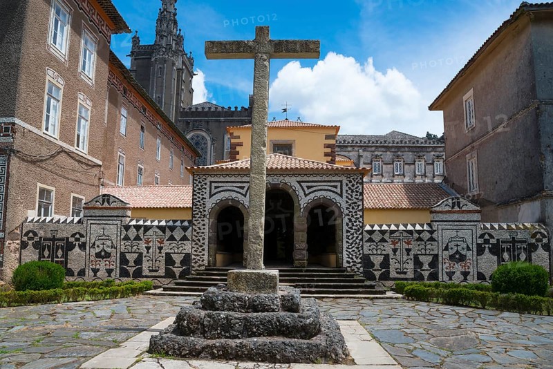 Ein altes Steinkreuz steht im Hof vor einem Mosaikdekorierten Gebäude unter blauem Himmel, ehemaliges Klosters, Convento de Santa Cruz, Mata Nacional do Buçaco, National-Wald von Bussaco, Bucaco, Mealhada, Beira Litoral, Portugal, Europe