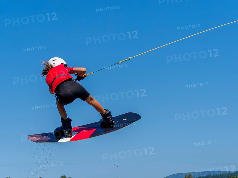 Boy or girl, jump with wakeboard over the lake, red life jacket and water sports, water skiing in the wake park