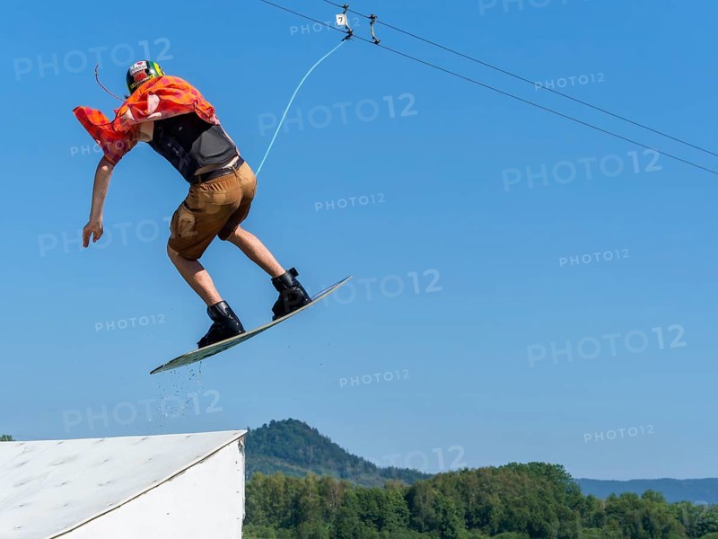 Young casual man with flapping shirt on wakeboard jumping over jump into the lake, water ski and wakepark, Stráž pod Ralskem, Czech Republic, Europe