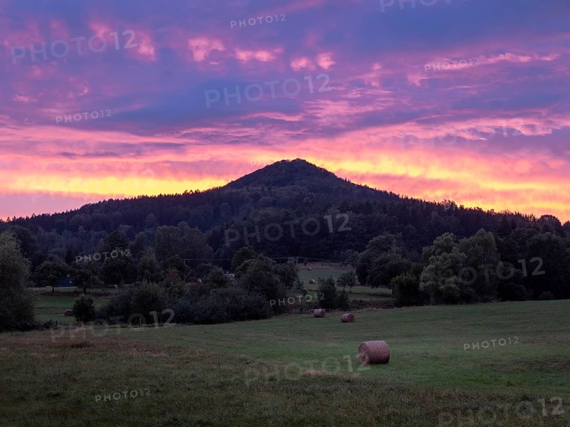 Meadows with straw bales in front of a mountain in the evening light with red sky, Sokol, Lusatian Mountains, Czech Republic, Europe