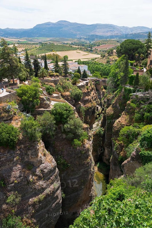 Deep ravine with green vegetation surrounded by white buildings and mountain landscape in Ronda, view from El Puente Nuevo, the new bridge, old town, Ronda, Málaga province, Malaga, Andalucia, Spain, Europe