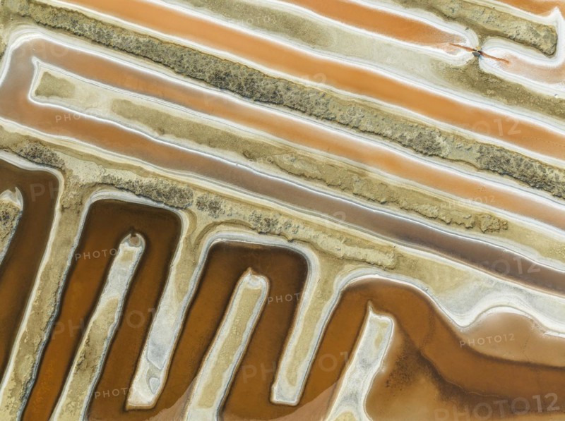 Saline ponds at the salt works near Chiclana de la Frontera. The orange-red colour depends on the level of salinity and is directly caused by the algae Dunaliella salina and brine shrimp. Aerial view. Drone shot. Cádiz province, Andalusia, Spain, Europe