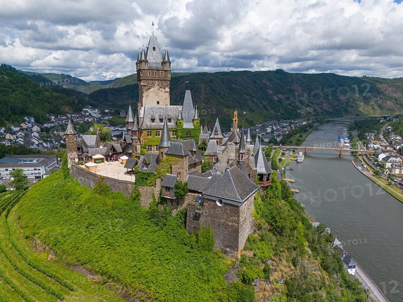 Medieval castle on a hill overlooking a river and a town, embedded in green nature and surrounded by mountains under a cloudy sky, aerial view, Reichsburg, Cochem, Cochem-Zell, Moselle, Rhineland-Palatinate, Germany, Europe