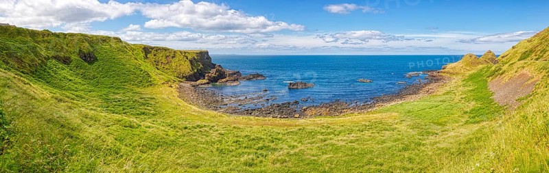 Green meadows meet the coast with a view of the sea under a blue sky, Giant Causeway