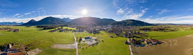 Aerial view of a village in a mountainous landscape under a bright blue sky, Bad Feilnbach