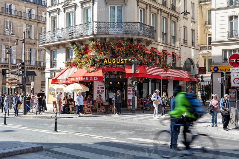 Snapshot of a lively street café with lush flower arrangements and cyclists, Paris