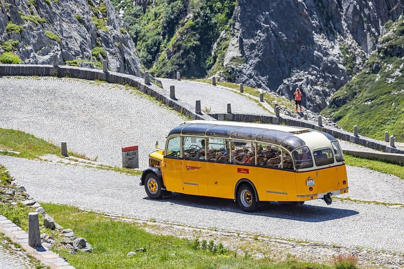 Historic postbus travelling along the Tremola, the world-famous serpentine road through the Val Tremolo. Tourist bus on the Tremola road, Switzerland's longest road construction monument with 24 hairpin bends. Airolo, Canton Ticino, Switzerland, Europe