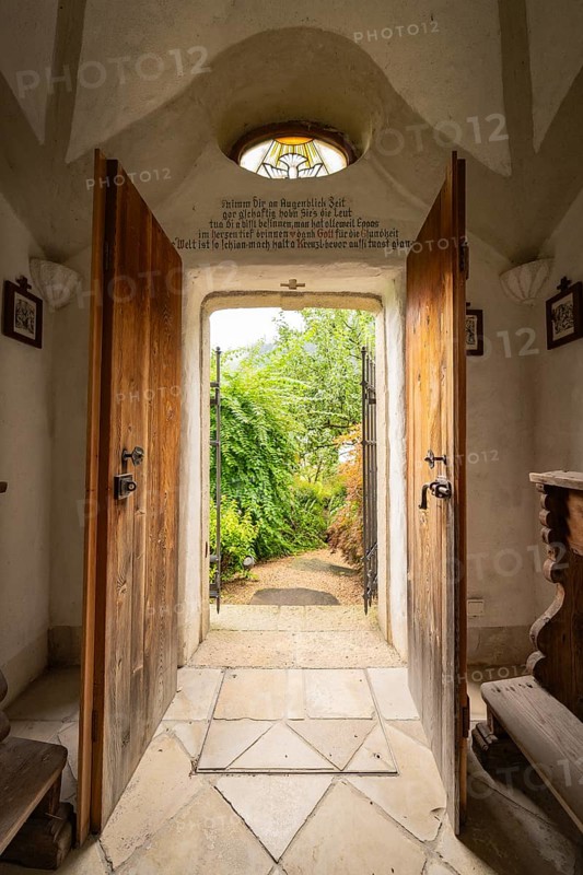 View through a historic entrance with stone floor into a green garden surrounded by wall art, Mayrhofen, Zillertal, Austria, Europe