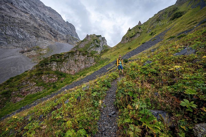 A mountaineer on a mountain path with lush green vegetation in foggy weather, hiking trail to Valentintörl, cloudy mountain peaks, Carnic Alps, Carnic High Trail, Carinthia, Austria, Europe