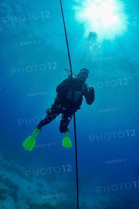 Diver making a safety stop in deep blue water with the sun shining above her. Dive site Punta Negra, Las Galletas, Tenerife, Canary Islands, Spain, Europe
