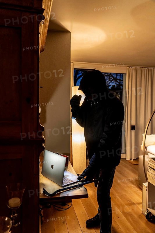 Symbolic image of a burglary, perpetrator has broken into a flat from the garden side and is looking for loot, computer, laptop, valuables, money, technology
