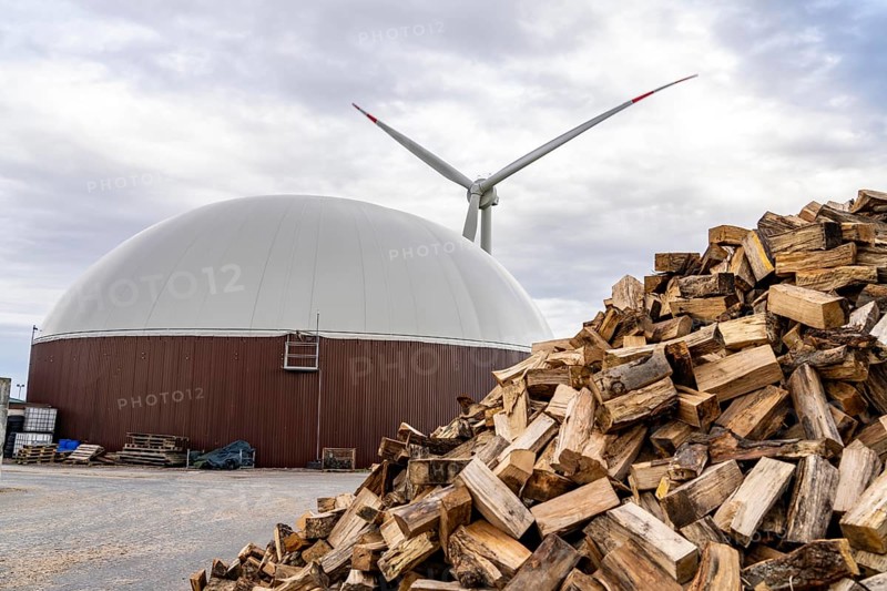 Biogas plant produces gas from various biomass, here the wood storage, the electricity is produced in combined heat and power plants with the biogas produced and sold to companies in the neighbouring industrial estate, the heat generated is fed into a local heating network, gas storage and wind power plant, Ense, North Rhine-Westphalia, Germany, Europe