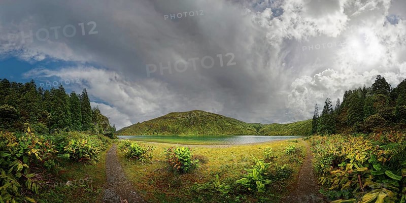A panorama of a green, forested landscape with mountains under a dramatically cloudy sky, crater lake Lagoa do Fogo, Caldeiras, Sao Miguel Island, Azores, Portugal, Europe