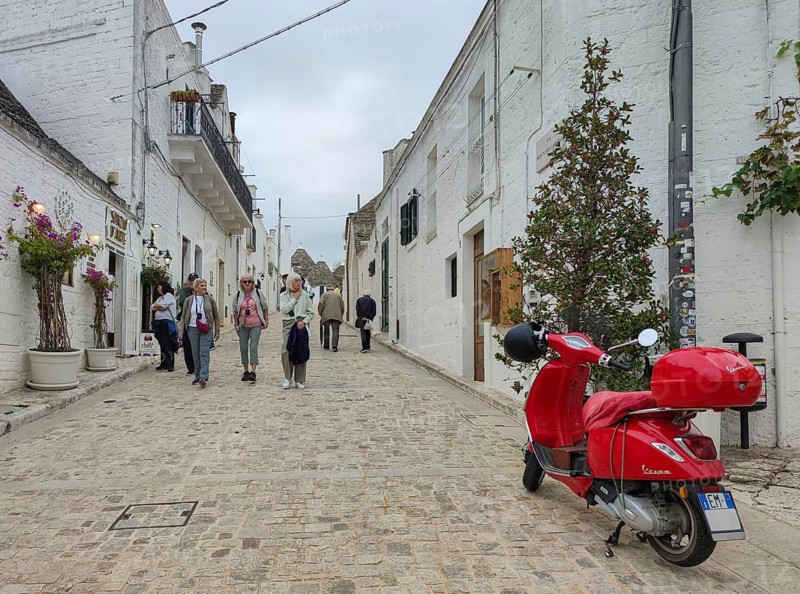 A picturesque street with white buildings, a red Vespa and people walking along, Alberobello, UNESCO World Heritage Site, Apulia, Italy, Europe