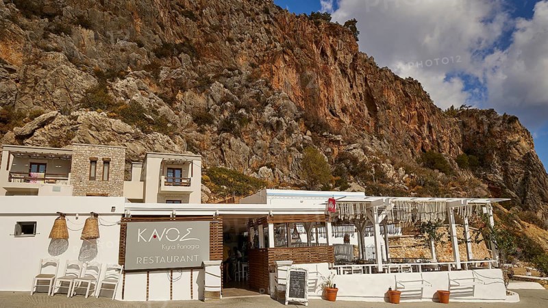 A restaurant in front of striking rocky cliffs with traditional stone architecture and wooden panelling under a clear sky, Kyra Panagia, Kyra Panagia Beach, East Coast, Karpathos, Dodecanese, Greek Islands, Greece, Europe