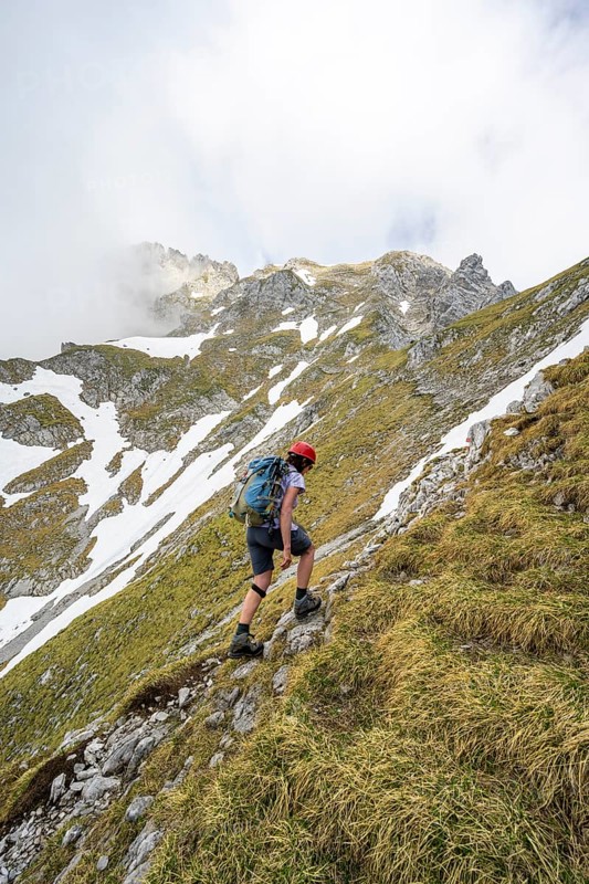 Mountaineer with helmet on a narrow hiking trail, ascent to the Ackerlspitze, clouds moving around the mountains, Wilder Kaiser, Kaiser Mountains, Tyrol, Austria, Europe