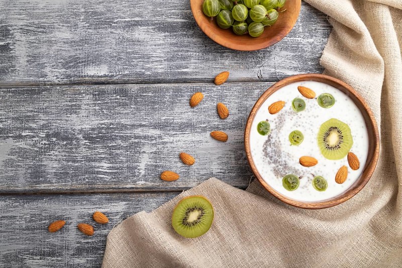 Yogurt with kiwi, gooseberry, chia and almonds in wooden bowl on gray wooden background and linen textile. top view, flat lay, copy space