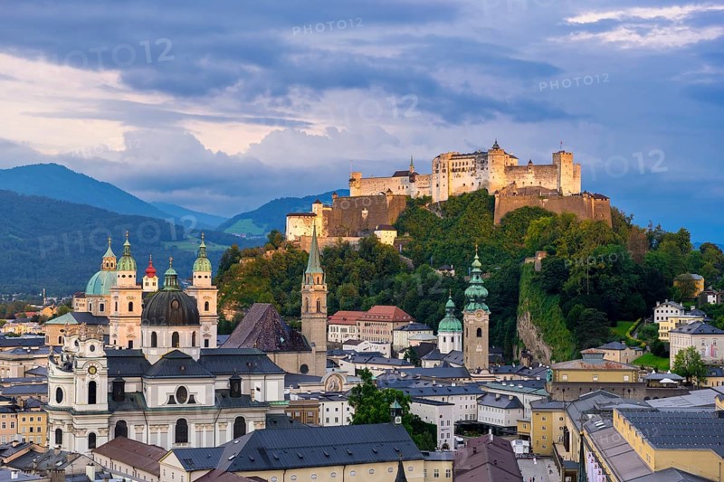 The illuminated Hohensalzburg Fortress towers above the city of Salzburg in the evening, surrounded by the Alps Salzburg, Salzburger Land, Austria, Europe