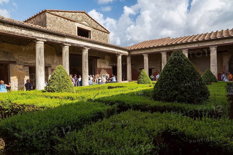 Tourists visiting a large old building designed with an inner garden courtyard and maze at the ancient ruins of Pompeii, Campania region, Italy, Europe