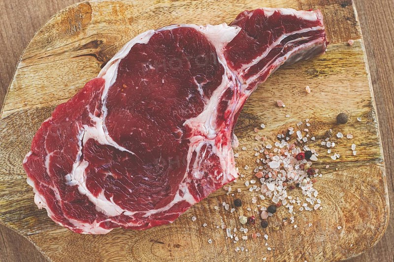 Raw rib eye steak, cowboy steak, on a wooden chopping board, top view, no people