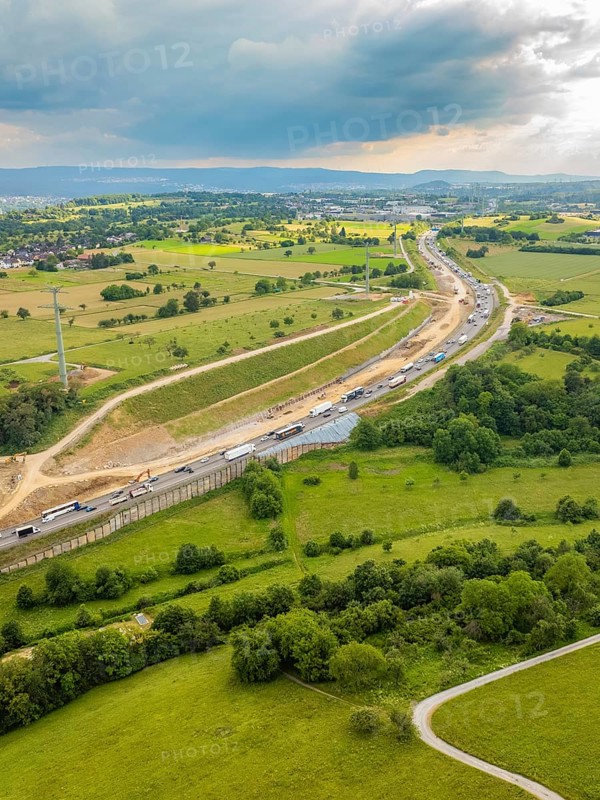 View of a large construction site next to a road through green fields and under a cloudy sky, A8 motorway, Kieselbronn, Germany, Europe