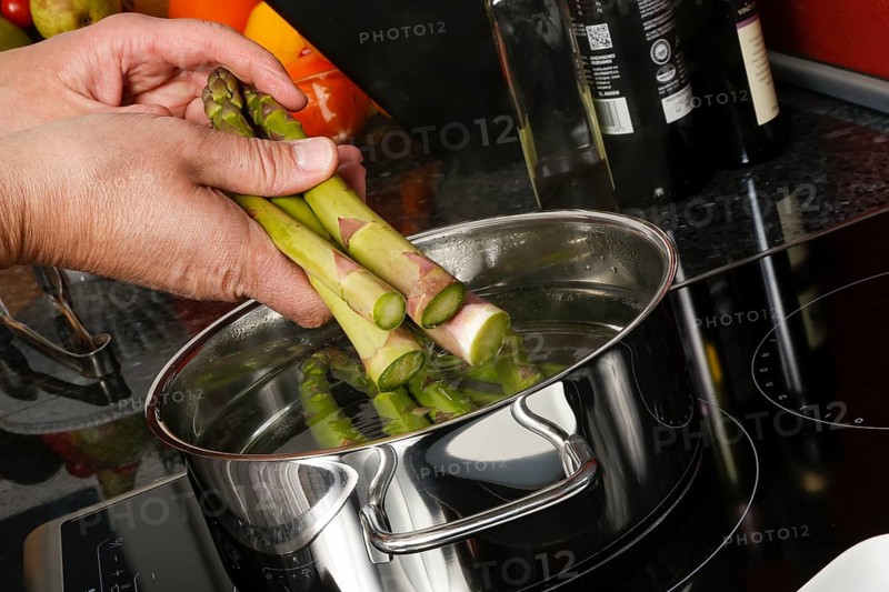 South German cuisine, vegetables, vegetarian, preparation of green asparagus with rhubarb vinaigrette and potato gratin, add raw asparagus to cooking water, saucepan, cooking sheet, induction cooker, ceramic hob, healthy, traditional cuisine reinterpreted, men's hands, food photography, studio, Germany, Europe