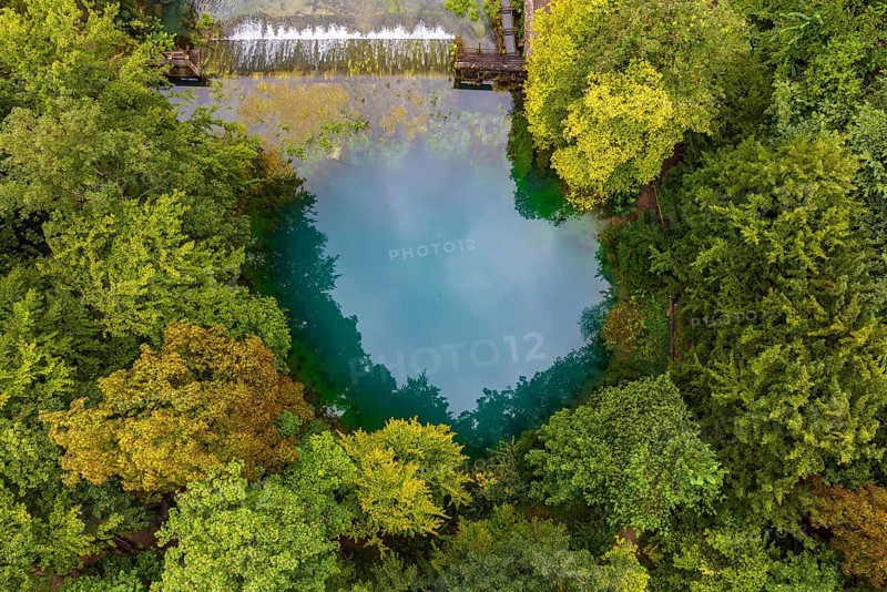 Blautopf Blaubeuren, source of the River Blau in a landscape with forest. Karst spring, geotope and geopoint of the UNESCO Swabian Alb Geopark, tourist attraction. The popular excursion destination is now being thoroughly renovated and will therefore be closed to visitors until the end of 2028. Drone photo. Blaubeuren, Baden-Württemberg, Germany, Europe